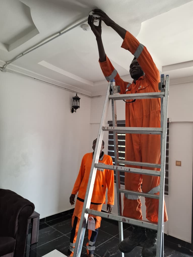 Installer fitting a ceiling smoke detector from a step ladder